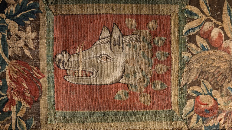 Detail of a tapestry showing a boar's head facing left with garlands of flowers to the left and right